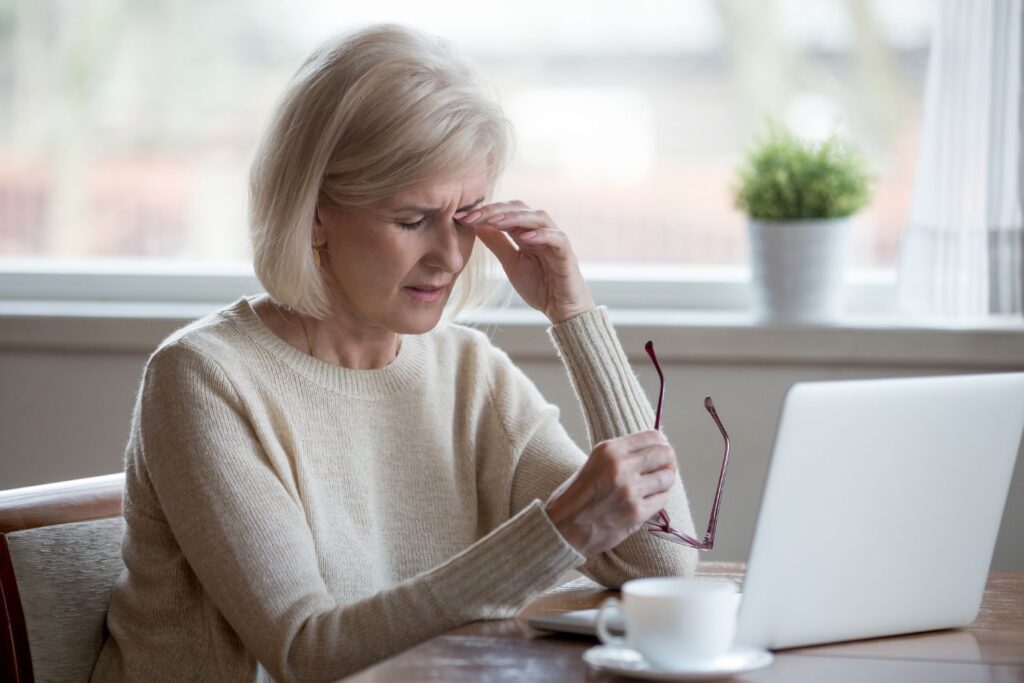 Conséquence de la ménopause au travail : impacts et astuces 2 Une femme agrée se tient la le haut du nez avec des lunette dans l'autre main pour illustrer les conséquences de la ménopause au travail