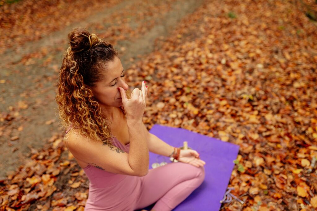 Respiration alternée ménopause : mini-routine zen anti-stress 1 Une femme habillée en rose position du lotus fait un exercice de respiration alternée menopause à l'extérieur
