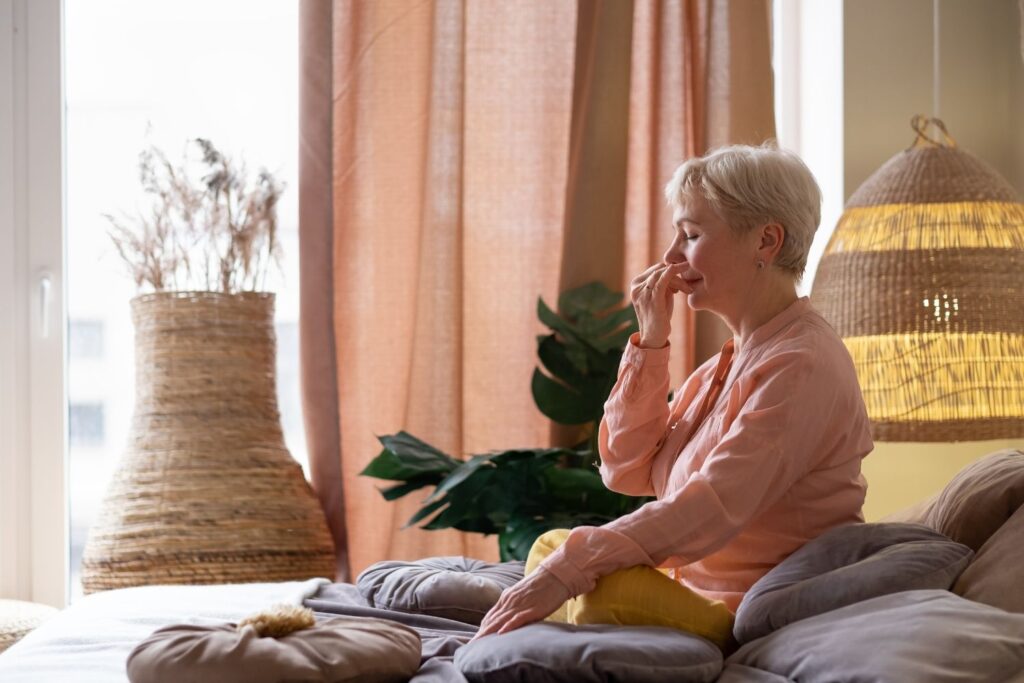 Respiration alternée ménopause : mini-routine zen anti-stress 2 une femme agée est assise en tailleur et presse sa narine pour faire un exercice de respiration alternée menopause