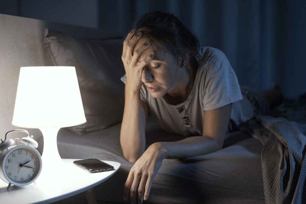 Ménopause et troubles du sommeil : pourquoi nos nuits partent en vrille (et comment les récupérer) 1 Ménopause et troubles du sommeil femme qui se tient la tete au dessus de la lumière