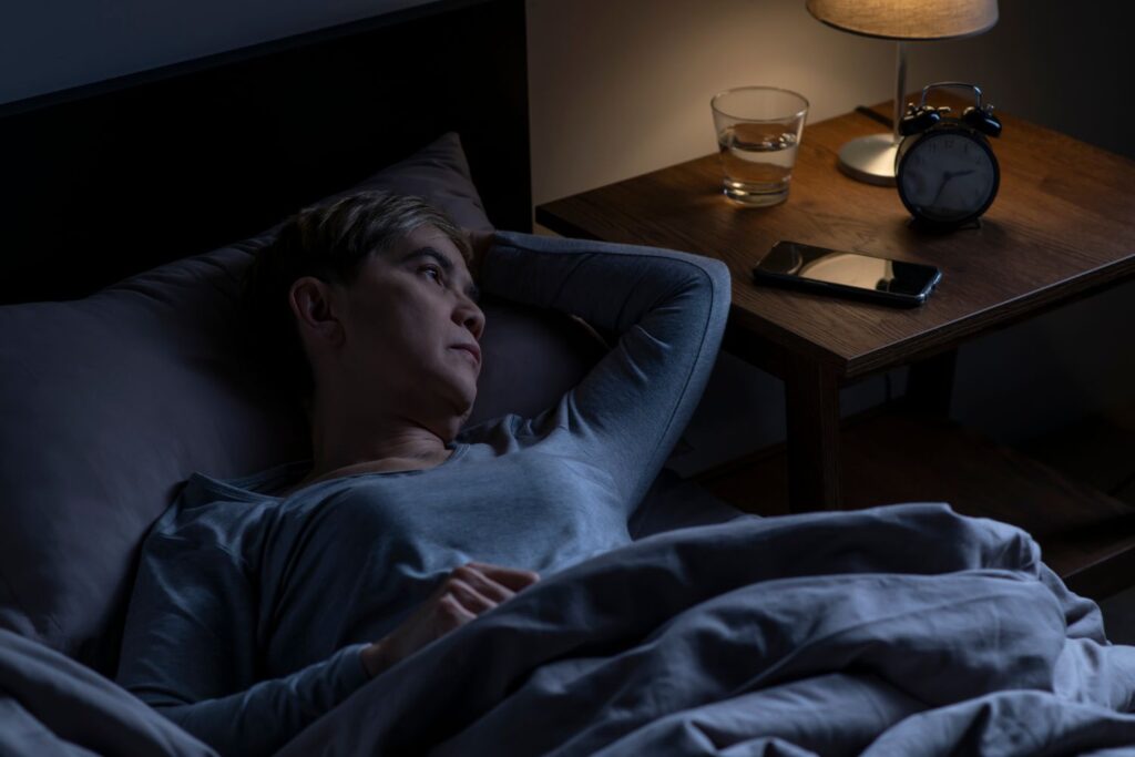 Ménopause et troubles du sommeil : pourquoi nos nuits partent en vrille (et comment les récupérer) 5 femme dans le noir les yeux ouverts qui vit la ménopause et troubles du sommeil