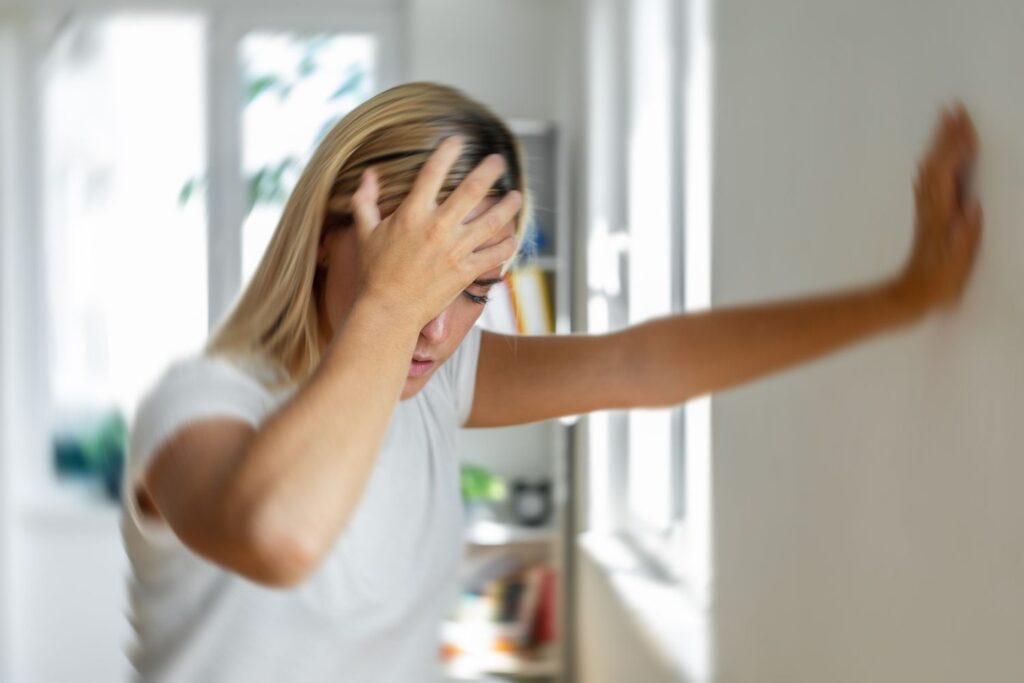 Ménopause et vertiges : signes d’alerte et bons gestes 3 Une femme se tient la tête d'une main et le mur de l'autre pour illustrer l'article ménopause et vertiges
