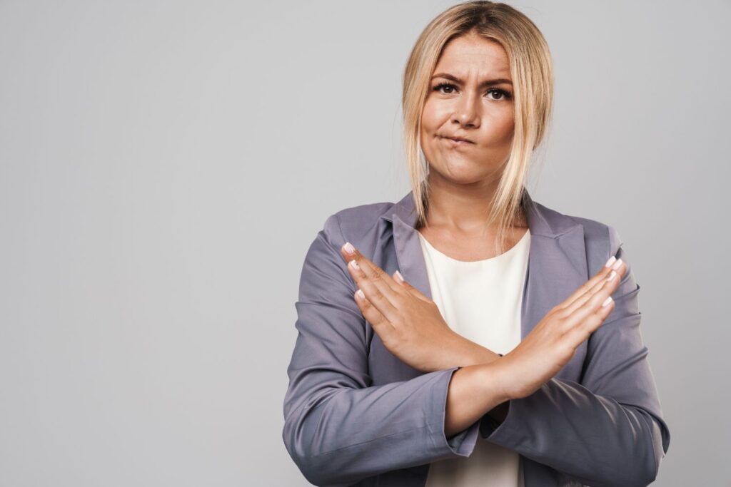 Votre outil gratuit pour suivre vos symptômes de la ménopause 5 Une dame blonde habillées en fris et blanc dit non avec ses bras pour parler de ce qu'il ne faut pas faire dans le cadre du suivi des symptômes de la ménopause
