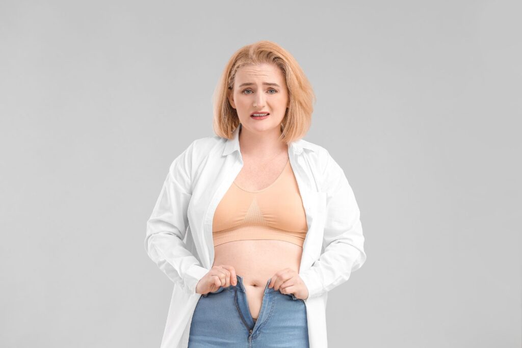 Ménopause : guide complet pour comprendre et mieux vivre cette étape de vie 4 une femme l'air dépitée essaye de fermer son jean trop serré pour l'article perte de poids à la ménopause