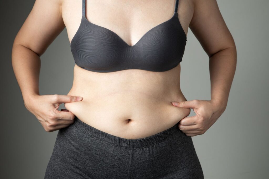 Perte de poids à la ménopause : stratégie douce et durable 1 une femme en sous vetements tiens ses bourrelets sur son ventre pour l'article perte de poids à la ménopause