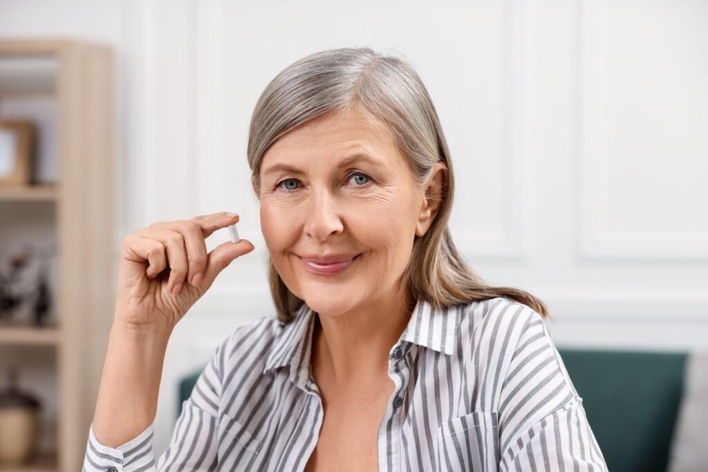 Traitement hormonal substitutif : l’ABC sans prise de tête 3 une femme d'age mûr cheveux gris tient une comprimé entre ses doigts pour illustrer l'article traitement hormonal substitutif