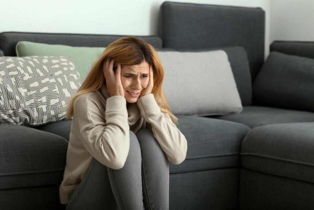 une femme rousse porte un legging gris assise par terre se tien la tête avec le visage crispé pour illustrer l'article angoisse et menopause