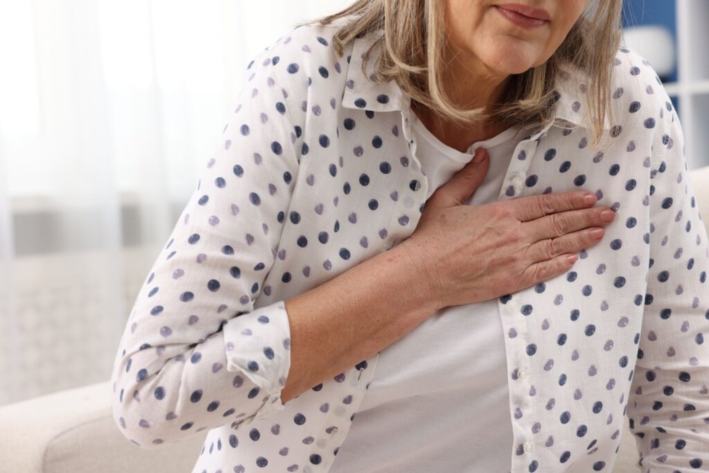 Une femme blonde d'age mur avec une chemise noir et blanc à pois a la main posée sur la poitrine pour calmer une crise de panique