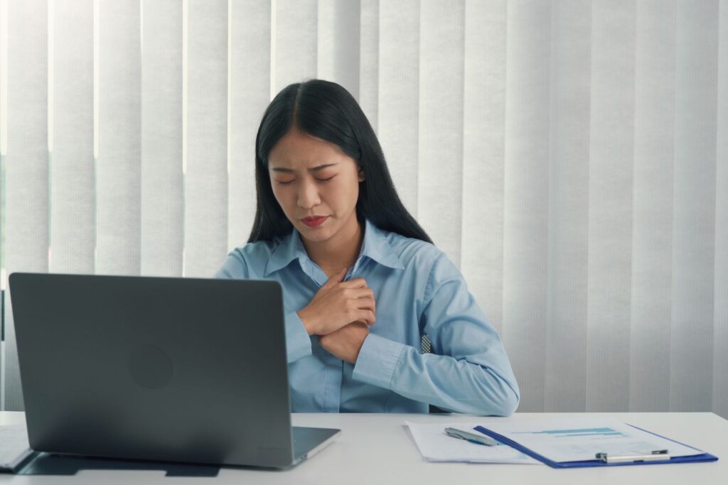 une femme se tient la poitrine assise devant son ordinateur et son bureau semble victime d'une crise d'angoisse
