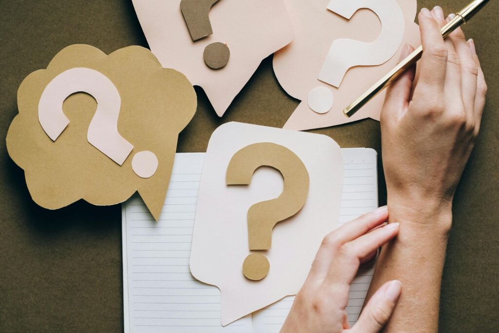 Des points d'interrogation en papier sur une table avec les mains d'une femme pour illustrer les questions que se posent les femmes sur leurs douleurs articulaires à la ménopause