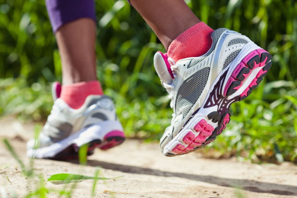 Des baskets roses blanches et grises portées par une personne qui marche pour illustrer des douleurs articulaires à la ménopause qui peuvent être soulagées par la marche.
