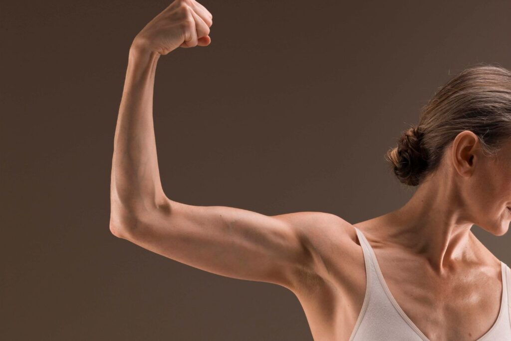 un bras avec le biceps contracté d'une femme aux cheveux gris pour illustrer l'article ménopause et sport