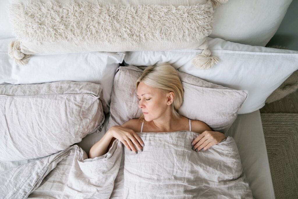 Une femme blonde dort paisiblement dans son lit sous ses draps pour illustrer l'article ménopause et sport