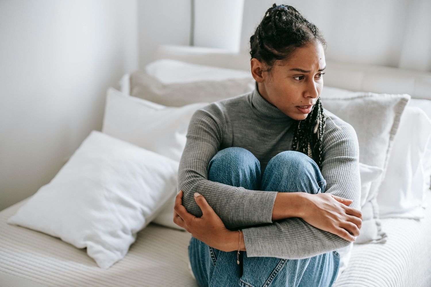 une femme la trentaine en jean avec un haut gris assise sur un lit l'air anxieuse pour illustrer l'article anxiété en périménopause