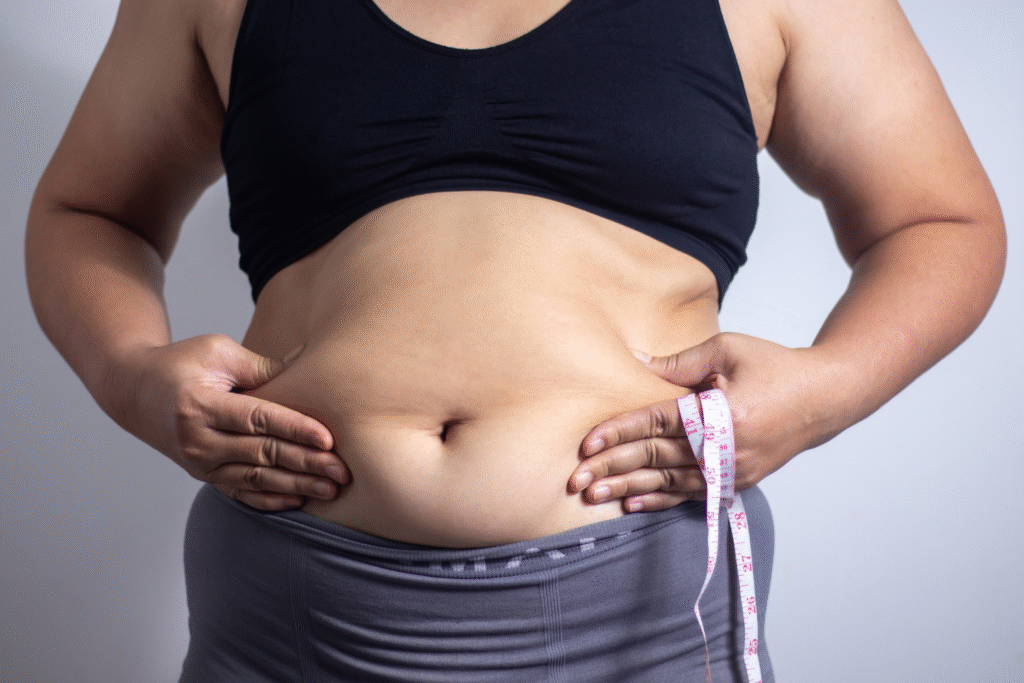 une femme en sous vêtement de face tient un mètre dans la main et pince la graisse de son ventre pour illustrer l'article gros ventre à la ménopause