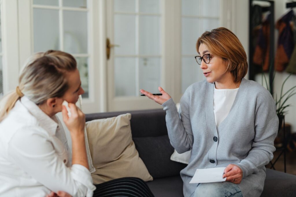une femme qui porte de lunettes habillée en gris clair qui explique des choses, à une autre par le geste pour illustrer l'insomnie à la ménopause
