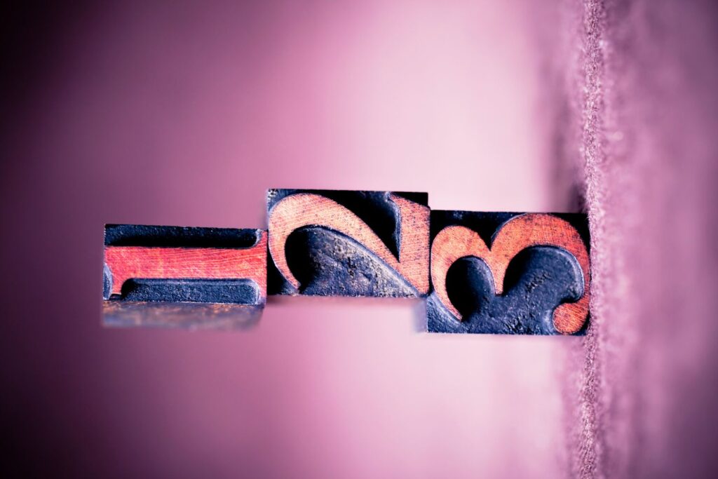 des cubes en bois & é " posés à l'horizontale sur un fond rose pour illustrer l'article peau sèche à la ménopause