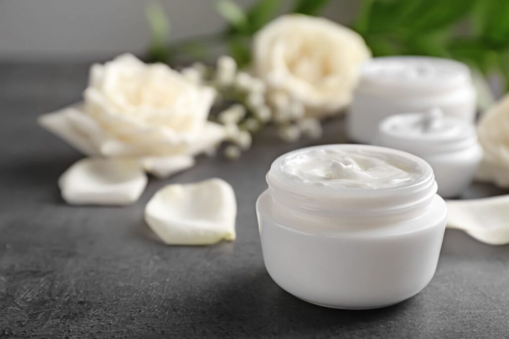 Un pot de crème de soin posé sur un support gris avec des fleur blanches en arrière plan pour illustrer l'article peau sèche à la ménopause