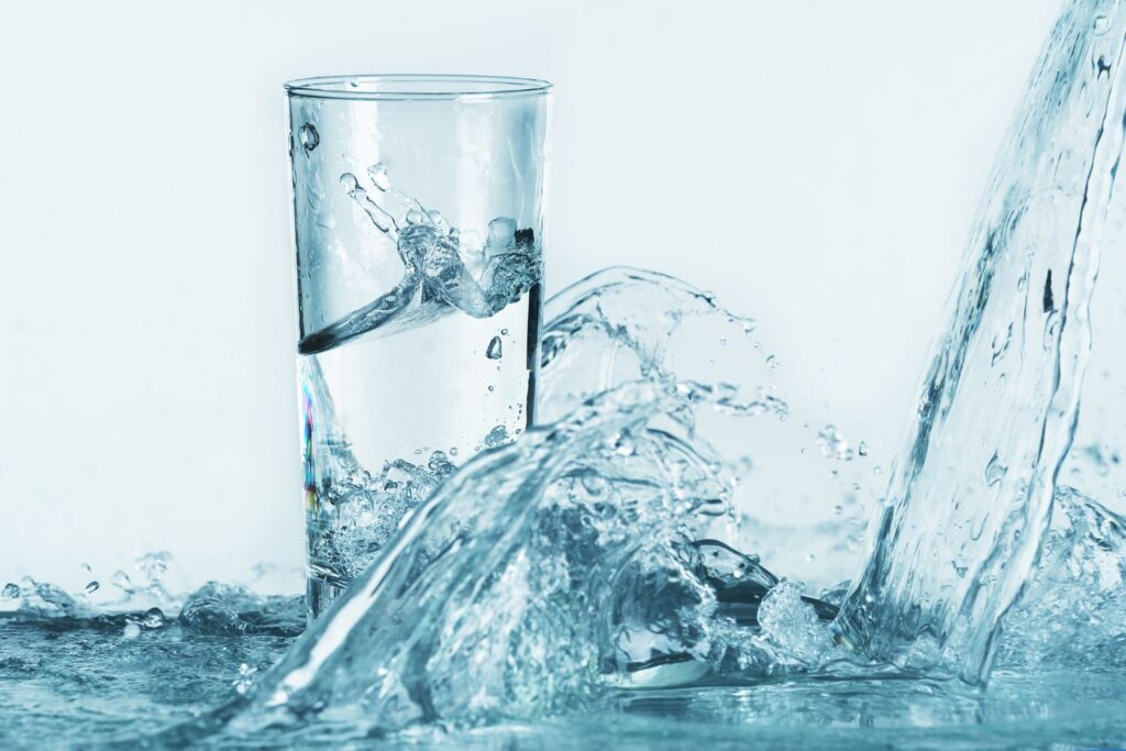 Un verre d'eau posé dans une flaque d'eau sur un fond bleuté pour illustrer l'article peau sèche à la ménopause