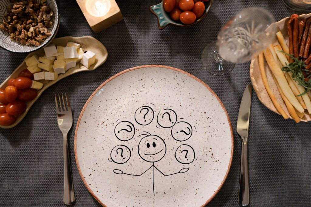 Une assiette vide avec des points d'interrogation à l'intérieurs avec des couvert de chaque coté et des aliment autour pour illustrer l'article quoi manger à la ménopause