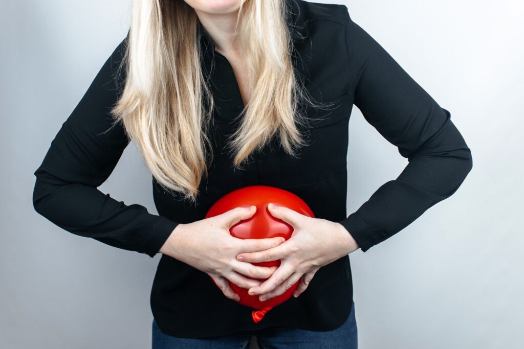 Femme blonde habillée en noir avec un ballon rouge gonflé sur le ventre pour illustrer l'article quoi manger à la ménopause