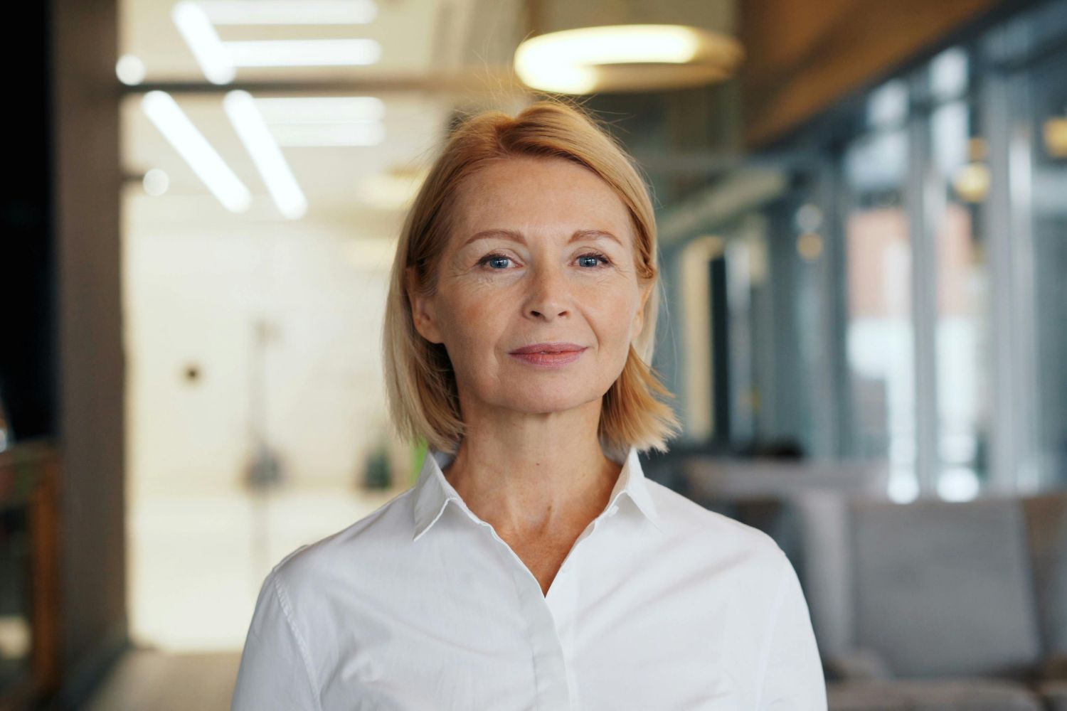 une femme la cinquantaine blonde porte une chemise blance et regarde l'objectif pour illustrer l'article sécheresse intime à la menopause, témoignage de Carole