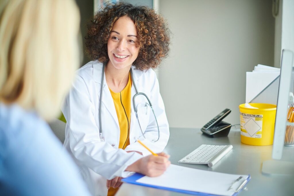 Un médecin femme en blouse blanche s'adresse a sa patiente blonde pour illustrer l'article sécheresse intime à la menopause, témoignage de Carole