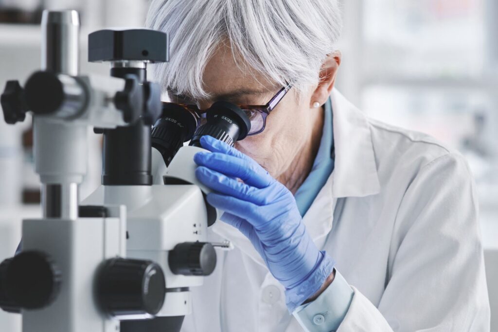 Une personne habillée en tenue médicale les cheveux gris penchée sur un microscope pour illustrer l'article sperme de saumon en injection.