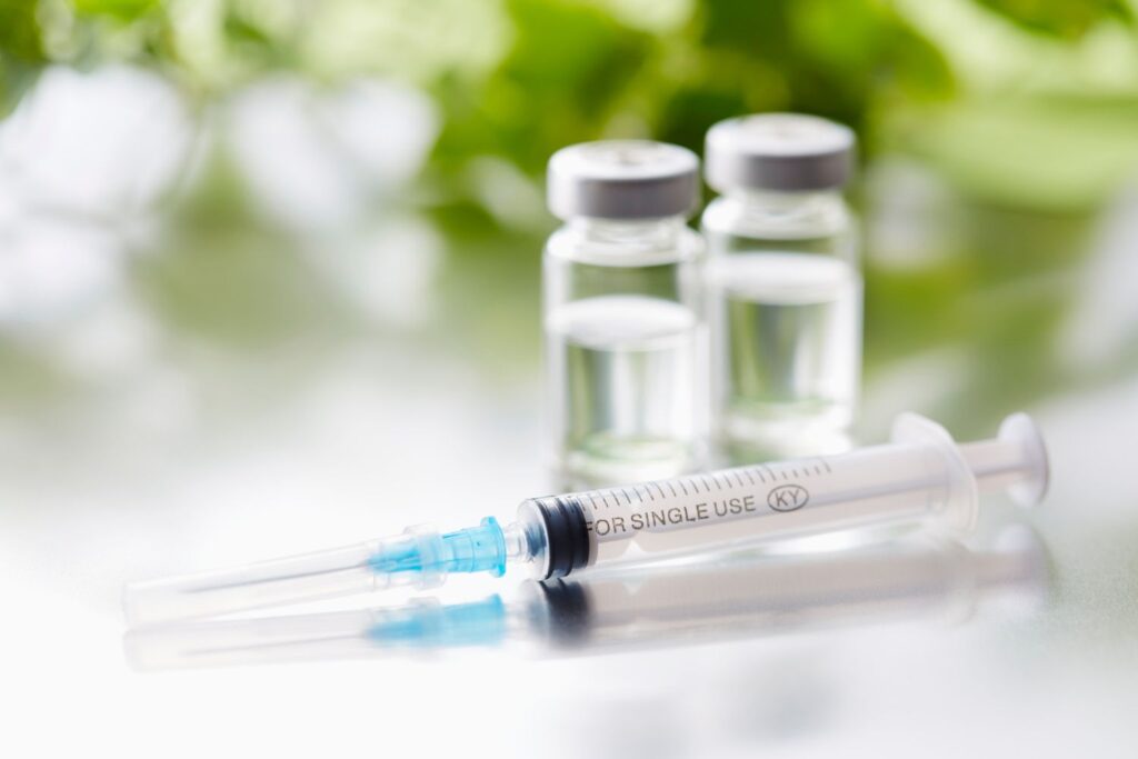 Une seringue à coté d'éprouvettes translucide s avec de la végétation en fond pour illustrer l'article sperme de saumon en injection.