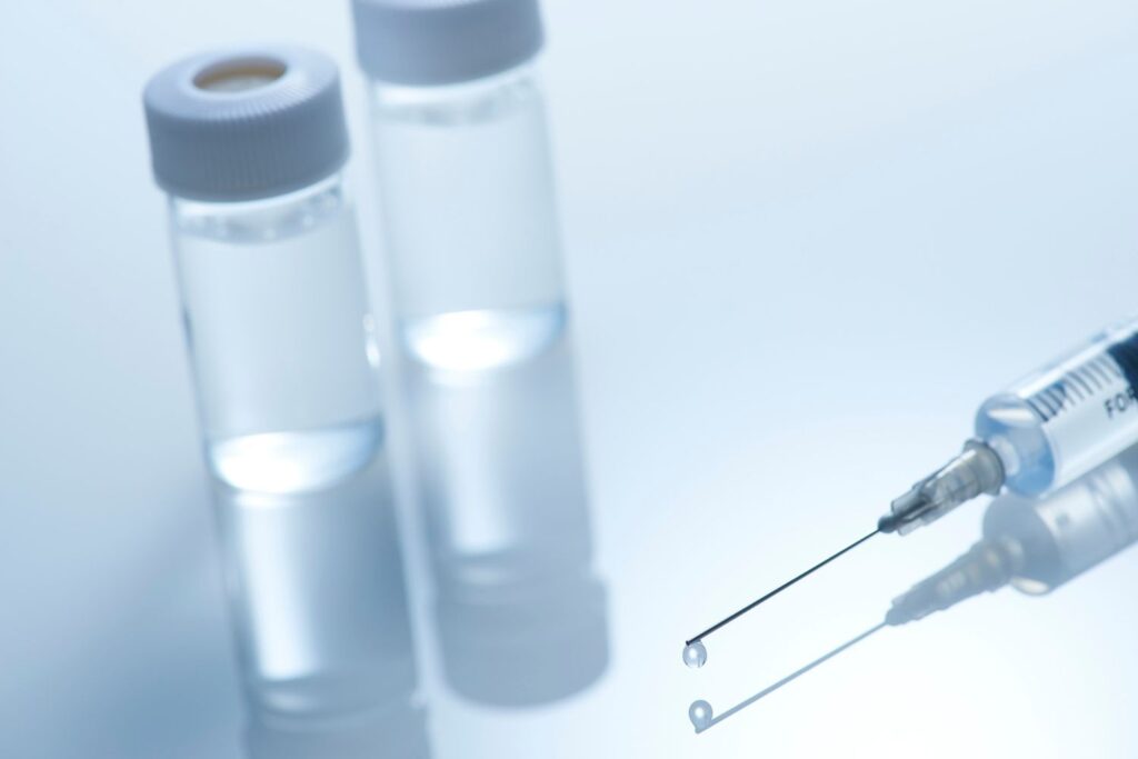 Une seringue a coté d'éprouvette contenant du liquide translucide sur un fond gris pour illustrer l'article sperme de saumon en injection.