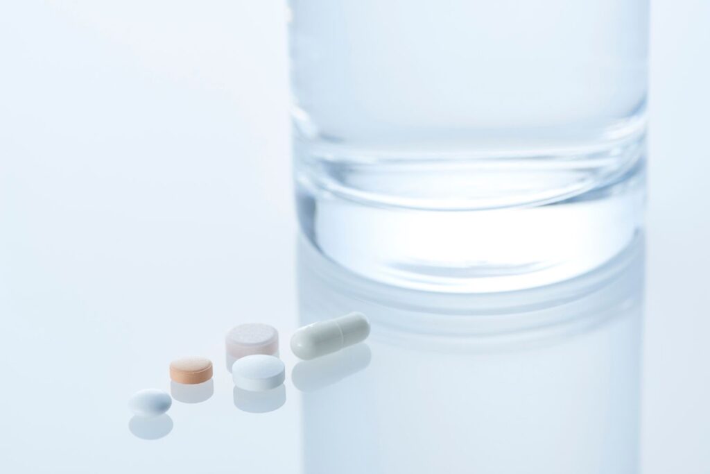 Quelques comprimés sur une table à coté d'un verre d'eau pour illustrer les médicaments pour la ménopause
