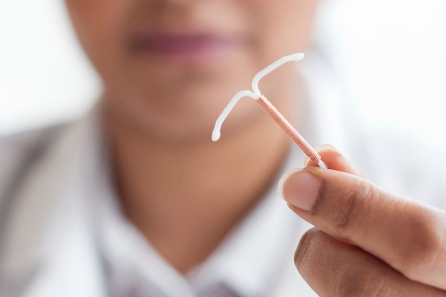 Un stérilet avec du cuivre et le bout blanc tenu entre deux doigt pour illustrer l'article comment savoir si on est ménopausée quand on a un stérilet