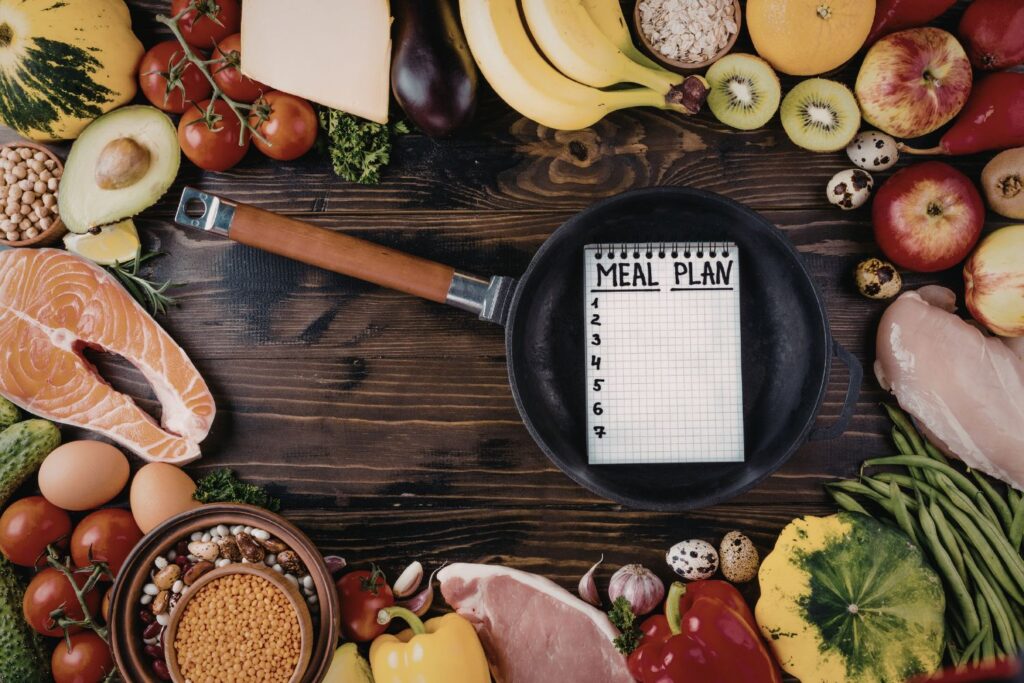 Un carnet de plan de repas posé sur un support en bois entouré d'aliments pour illustrer l'article alimentation à la ménopause