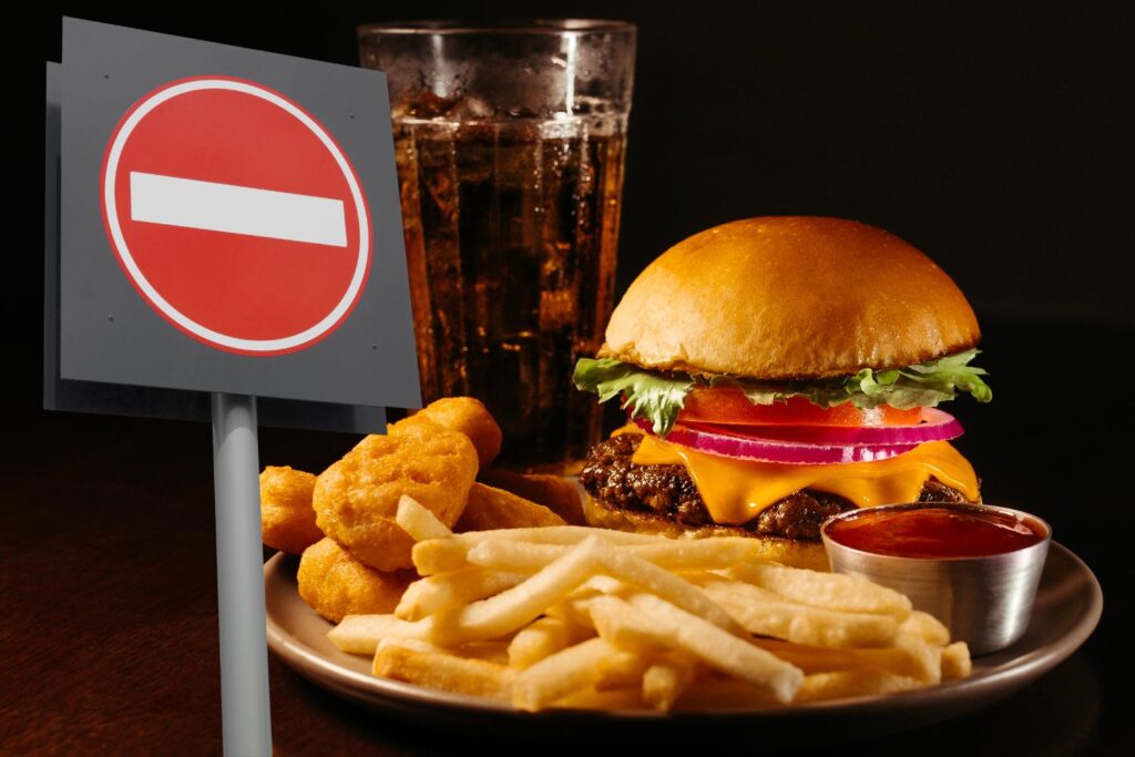 Un burger, der frites, une verre de coca avec un panneau interdit devant pour illustrer l'article alimentation à la ménopause