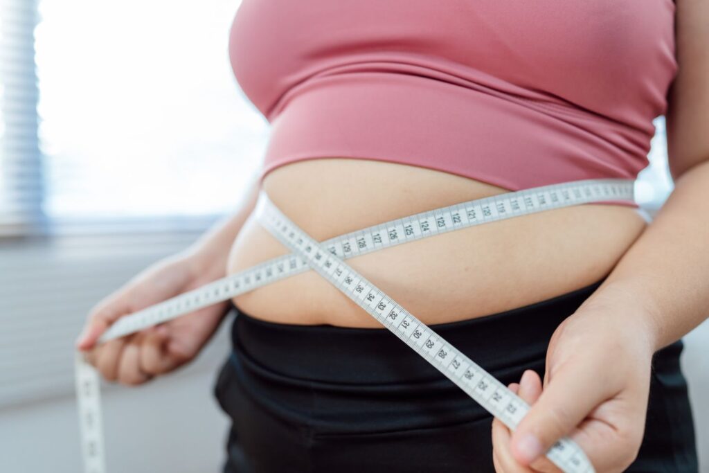 Le ventre d'une femme qui entoure son ventre gros et gonfle avec un mètre de couturière pour illustrer l'article ventre à la ménopause.